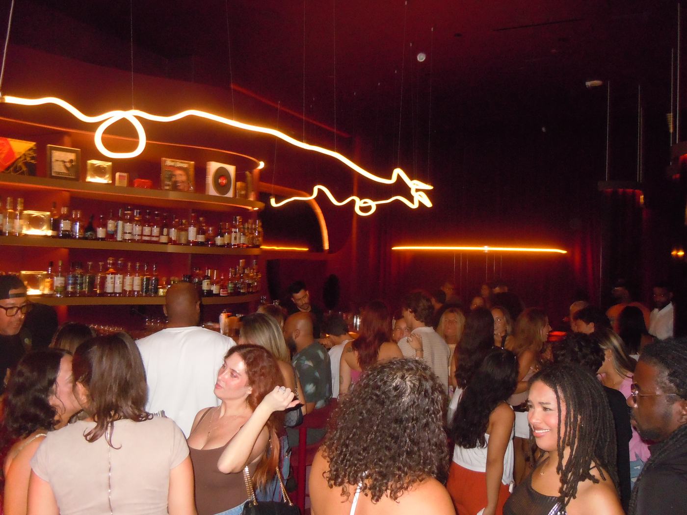 The bar at Alter Ego, lit by neon signage, with guests gathered around in Water Street Tampa